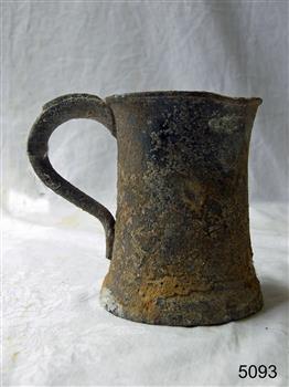 Grey metal tankard has a buckled lip and the surface is covered with encrustations