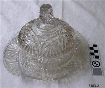 Moulded patterned glass butter dish with lid. Lid has knob on top. Base is broken.