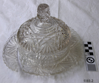 Moulded patterned glass butter dish with lid. Lid has knob on top. Base is broken.