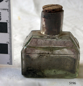Clear glass ink bottle with rectangular base and shoulders shaped for use as a pen rest