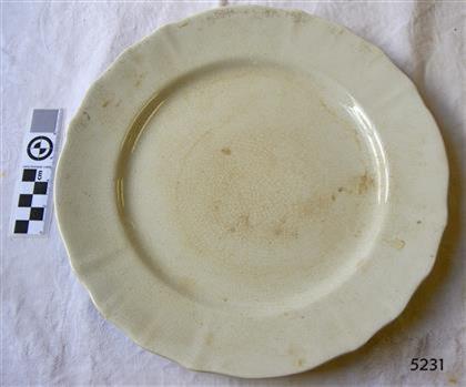 White earthenware scalloped dinner plate, partly discoloured.