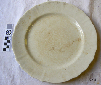 White earthenware scalloped dinner plate, partly discoloured.