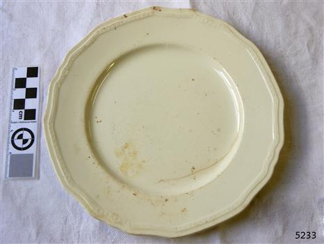 Cream earthenware scalloped dessert plate,  partly discoloured, and showing a significant crack.