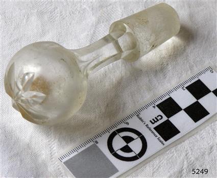 Glass bottle stopper's top has floral motif, neck is six-sided, stopper base is textured glass