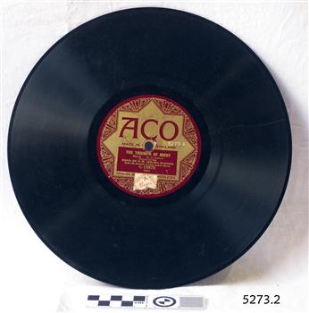 A flat black disc with spiralling grooves and a crimson and gold label around the central hole