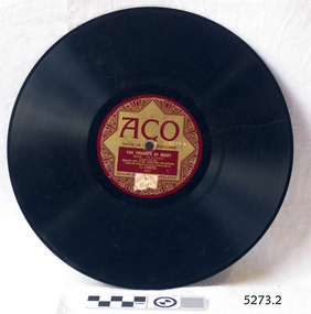A flat black disc with spiralling grooves and a crimson and gold label around the central hole