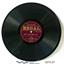 A flat black disc with spiralling grooves and a burgundy and gold label around the central hole