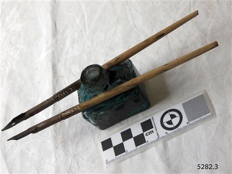 Boat-shaped ink bottle with cork, beside wooden pesn with metal nib.