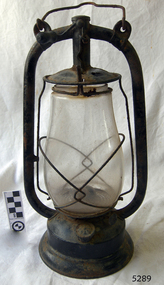 Lamp has metal frame with fuel tank at base. Glass is bulbous.