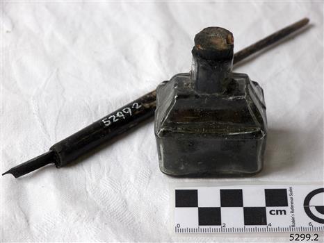 Boat-shaped ink bottle with cork, beside wooden pen with metal nib. Boat-shaped ink bottle with cork, beside wooden pen with metal nib.