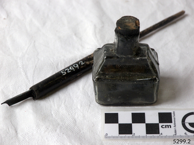 Boat-shaped ink bottle with cork, beside wooden pen with metal nib. Boat-shaped ink bottle with cork, beside wooden pen with metal nib.