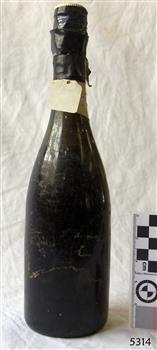 Dark coloured bottle has cap and sea in place. surface is scratched