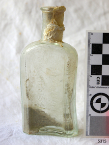 Clear glass bottle. Contains sediment. White encrustations on neck.