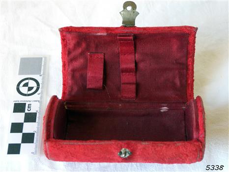 Chest-shaped box covered in crimson velvet with metal button closure. Fittings inside for items.
