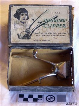 A cardboard box containing clippers, decorated with a sketched portrait of a female with short dark hair. 