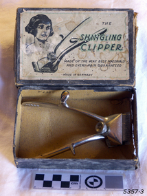 A cardboard box containing clippers, decorated with a sketched portrait of a female with short dark hair. 
