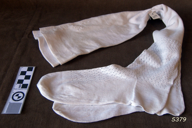 Long white handmade stockings with pattern on top of foot up to below the knee.