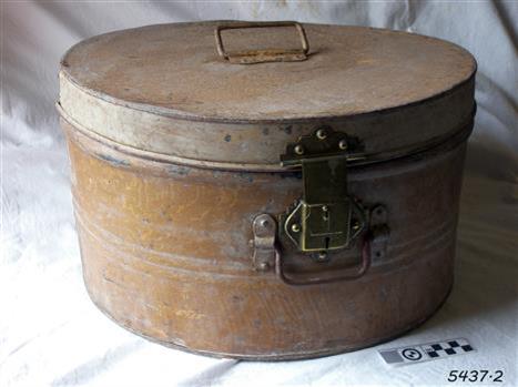 Round metal hat box, brown, with folding handle on lid and front, and a lockable catch on the front 