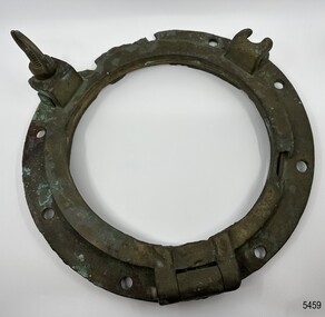 Brass porthole frame has hinge and fittings attached. There is damage to the metal.