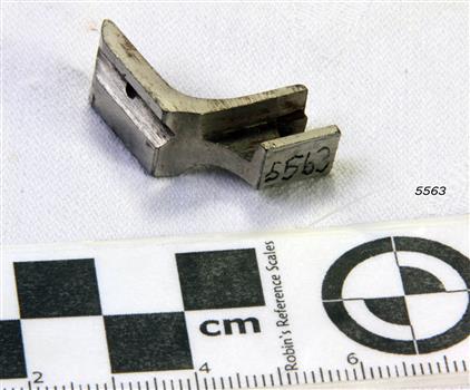 A metal 'L' shaped tool with grooves for fitting to machine and working with the fabric