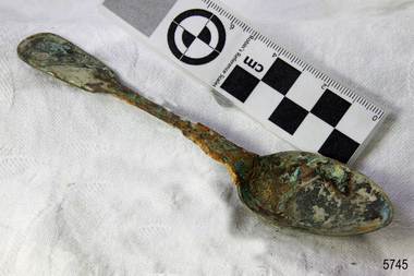 A large spoon golden in colour covered in black and green marks