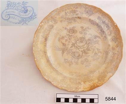 White ceramic plate, round with scalloped edge and blue floral design. Surface has a brown stain.
