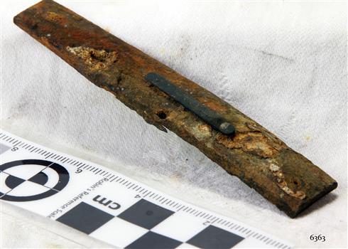 Rectangular shaped section with orange corrosion and drilled holes