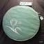 Round doily case covered in green fabric with white embroidered trim and floral motif