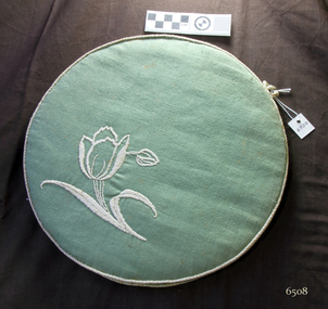 Round doily case covered in green fabric with white embroidered trim and floral motif