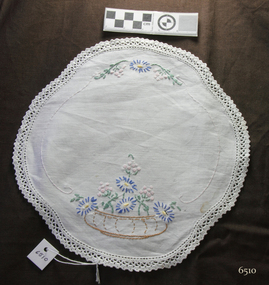 Scalloped ovate white doily embroidered with a shallow vase of blue and white flowers, edged with crochet 
