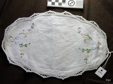 Oval white doily with embroidered flowers and crocheted edging