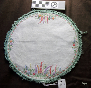 Round doily on white cotton with colourful floral embroidery and green crocheted edging