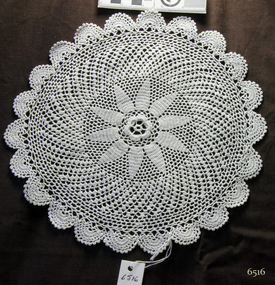 Round white doily, crocheted, with scalloped edges and flower motif in centre