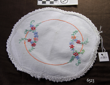 White cotton doily with red, blue, pink and orange floral embroidery and white crocheted border