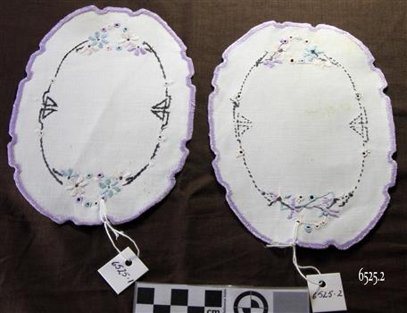 Pair of white oval doilies with brown embroidered border between blue and white floral embroidery. Crocheted mauve edge.