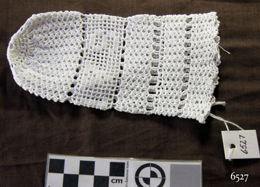 White crocheted sauce bottle cover, oblong and  drawn to a point at one end. Inscription worked into the pattern.