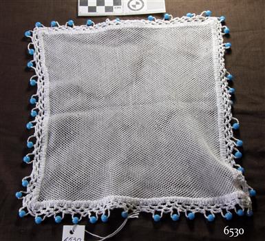 Square, white net jug cover with crocheted edge and blue beads attached along the borders