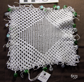 White crocheted square with central diamond pattern and alternate blue, green and clear beads on the border
