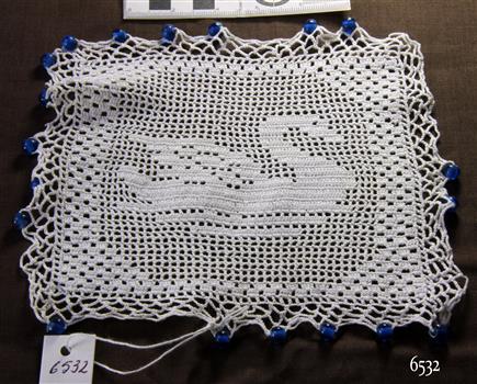 White square crocheted jug cover with edging of blue beads and swan motif incorporated in design
