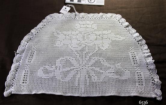 Half-circle shaped white crocheted tea cosy with floral design incorporated into the cover