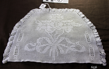 Half-circle shaped white crocheted tea cosy with floral design incorporated into the cover