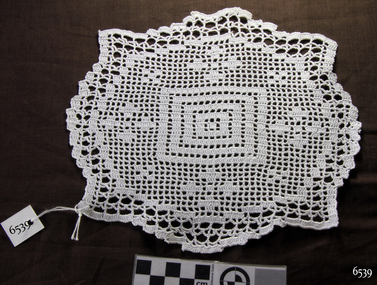 Crocheted white doily. Concentric squares in centre, with floral motifs in oval surround and pointed border