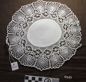 White oval doily with embroidered cotton fabric centre and wide crocheted border with leaf motif