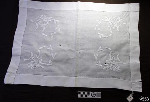 White rectangular cloth tray cover with wide hem and embroidered floral motifs in each corner