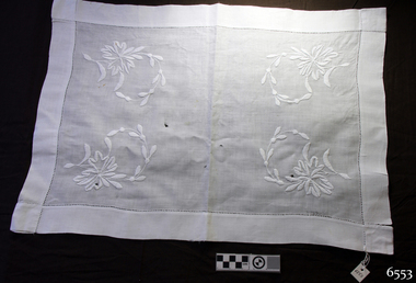 White rectangular cloth tray cover with wide hem and embroidered floral motifs in each corner