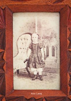 Studio photograph of a standing female child wearing short sleeved dress, pantaloons and sturdy shoes.