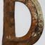 Front of metal letter D. Metal in the centre is higher than on the edges.