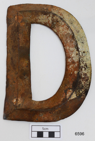 Front of metal letter D. Metal in the centre is higher than on the edges.