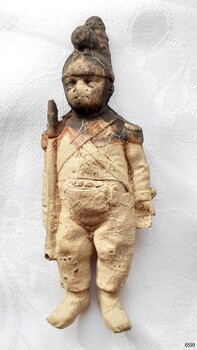 Cream figurine, unpainted, dressed as a soldier, holding a weapon. Stained surface.