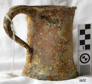 Upright mug of pewter with large handle and inward curved sides. Encrustations attached.